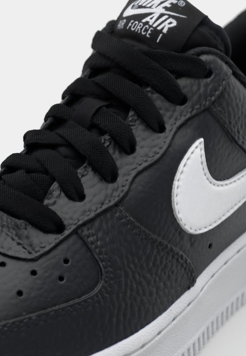 Die Nike Air Force 1 Sneakers verfügen über ein Obermaterial aus schwarzem strukturiertem Leder, einen weißen Leder Swoosh und schwarze Schnürsenkel mit einem Logo auf der Zunge.
