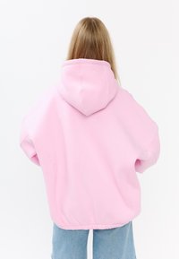 Felpa over-size rosa con cappuccio regolabile, orlo a costine e texture liscia. Presenta spalle scese e design minimalista.