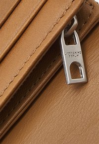 Portefeuille en cuir marron avec une texture lisse, présentant des coutures verticales et un tirette de fermeture éclair en argent marqué "LIEBESKIND BERLIN."