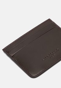 Ciemnobrązowy skórzany etui na karty o gładkiej fakturze, z czterema przegródkami na karty i wytłoczonym logo marki. Elegancki, minimalistyczny design z subtelnym przeszyciem.