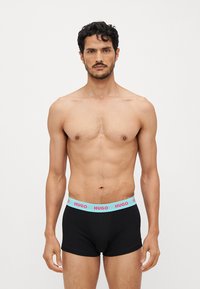 Schwarze Boxershorts mit einem hellblauen HUGO-Logo-Bund. Der Stoff wirkt glatt und dehnbar und passt sich der Körperform des Trägers an.