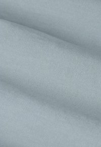 Tissu gris clair avec une texture lisse et un éclat subtil. La surface présente un motif de tissage fin et régulier avec un drapé doux.