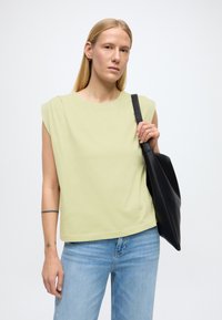 Haut sans manches vert clair, coupe décontractée, associé à un jean bleu taille haute et porté avec un sac fourre-tout noir. Design simple et minimaliste.