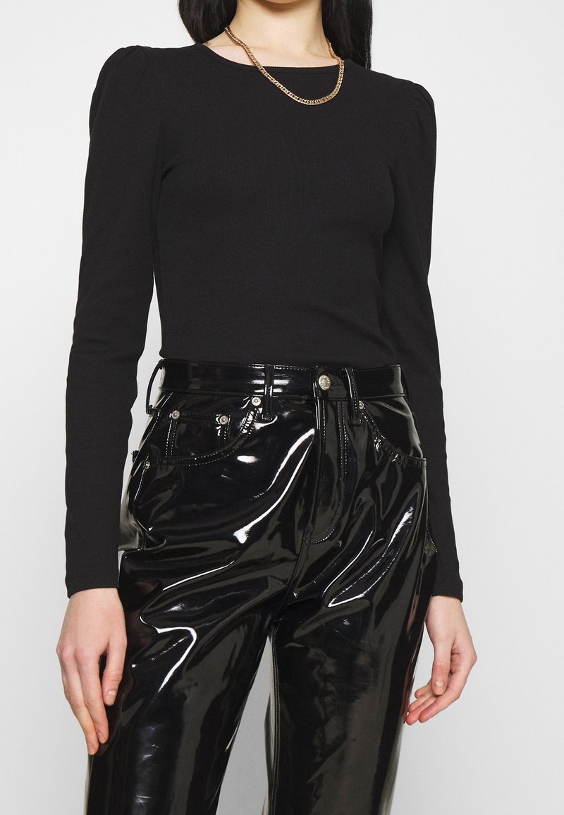 Haut noir à manches longues en maille côtelée avec épaules bouffantes, associé à un pantalon taille haute en faux cuir noir brillant avec poches décoratives et coutures.