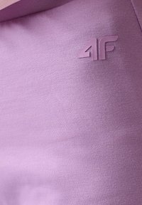 Gros plan sur un tissu lavande avec un logo en relief "4F" imprimé près du coin supérieur droit sur un matériau à texture lisse.