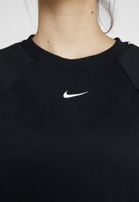 Gros plan d'une personne portant un sweat-shirt noir à col ras du cou avec un petit logo blanc Nike Swoosh au centre de la poitrine.