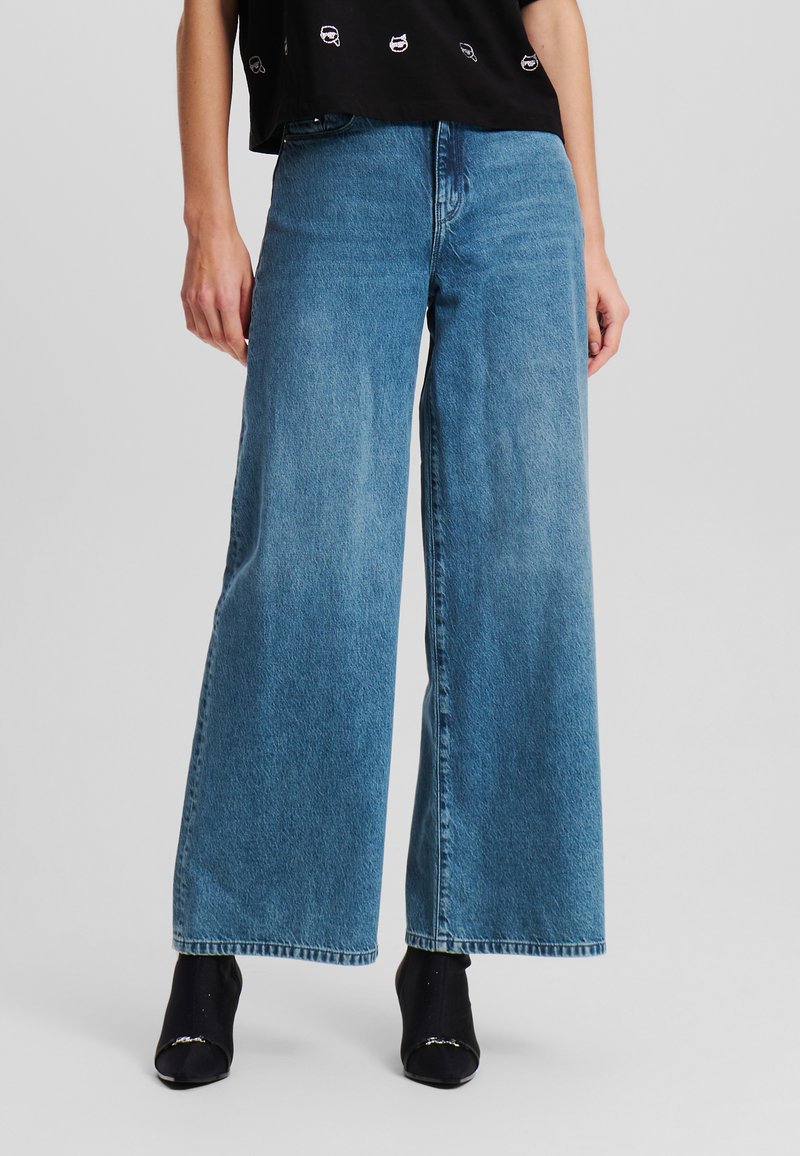 Helle blaue, weit geschnittene Denim-Jeans mit hoher Taille und einem sauberen Abschluss am Saum. Kombiniert mit schwarzen Stiefeletten und einem kurzen Oberteil.