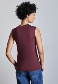Burgundy ärmlös topp med rund halsringning, tillverkad av ett slätt material, figursydd design, visad bakifrån mot en ljusgrå bakgrund.