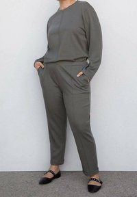 Cet ensemble deux pièces gris se compose d'un haut à manches longues avec un col rond et d'un pantalon fuselé assorti, tous deux dotés de poches latérales et d'une texture lisse.