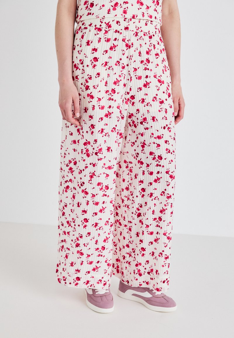 Pantaloni a gamba larga in tessuto bianco con stampa floreale rosa, caratterizzati da un design plissettato e una vita elastica. Abbinati a sneaker rosa.