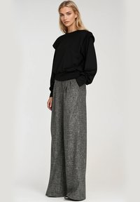 Czarny długi rękaw sweter z akcentami na ramionach, połączony z szerokimi szarymi spodniami w wzory. Gładki materiał z luźnym krojem.