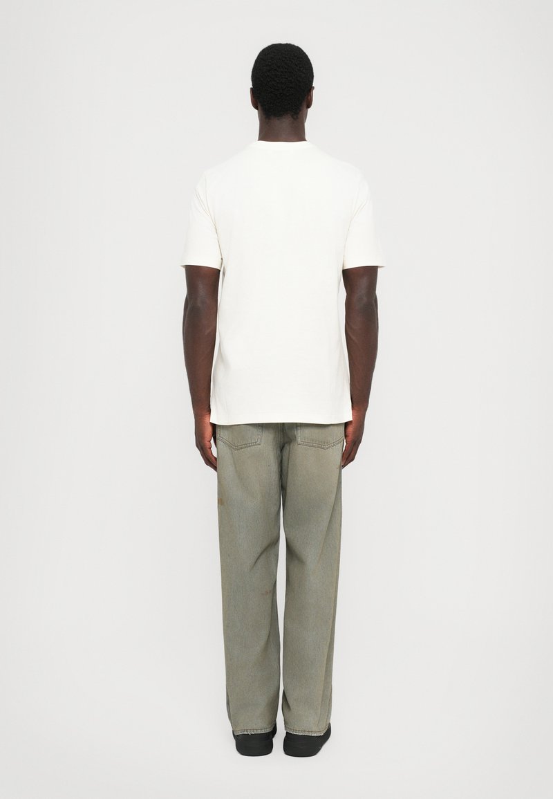 Cream cotton t-shirt with short sleeves, paired with loose-fitting, faded gray denim pants. The outfit has a relaxed fit and minimal detailing.
