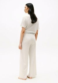 Jumpsuit in morbido tessuto grigio chiaro, con maniche corte, vestibilità ampia e cinturino elastico. Presenta gambe larghe e un design rilassato.
