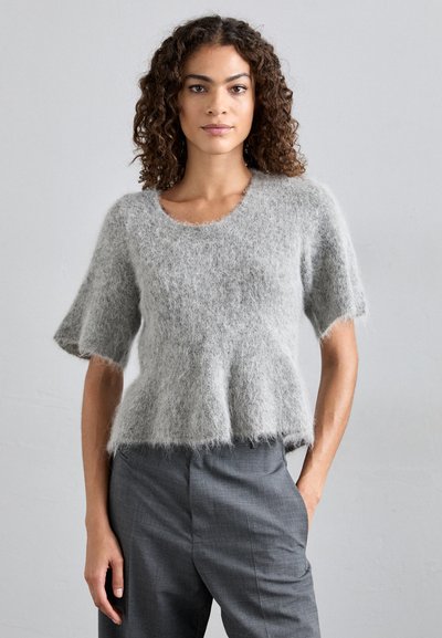 Γκρι, αφράτος κοντομάνικος πουλόβερ με στρογγυλή λαιμόκοψη και φούστα από κάτω, συνδυασμένο με γκρι κομμένα παντελόνια. Μαλακή υφή και χαλαρή εφαρμογή.