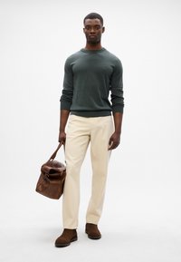 Mørkegrøn strikket sweater, cremefarvede bukser, brunt lædertaske og brune støvler. Simpelt design med ribbede manchetter og kant.