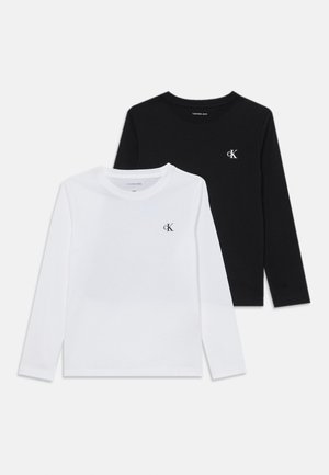 Twee langemouwen T-shirts van wit en zwart katoen, met een klein "ck" logo op de borst, ronde hals en een eenvoudig ontwerp.