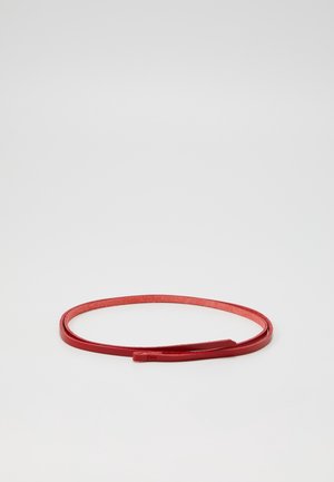 Tynd rød læderbælte lagt fladt i en løs sløjfe uden synlig spænde mod en hvid baggrund.