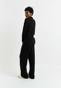 Pull en maille noir avec un col haut, texture côtelée et accent rouge contrastant à l'ourlet. Assorti à un pantalon large noir.