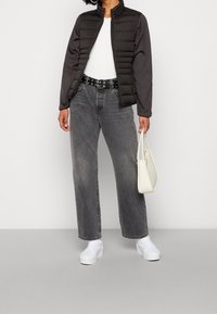 Giacca nera imbottita, camicia bianca a coste, jeans grigi a vita alta, cintura nera con accessori in argento, sneakers bianche e una piccola borsa bianca.