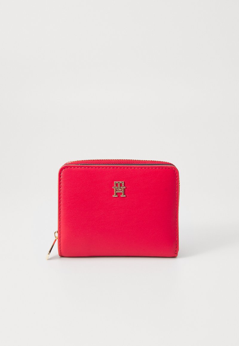 Red leather zip wallet with a textured finish, featuring a gold-tone logo on the front and a zipper closure. Compact rectangular shape.