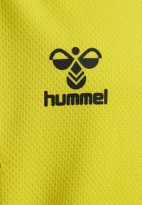 Gelbes Textil mit einem strukturierten Muster, mit einem schwarzen Logo über der Schrift "hummel" in einer fetten, modernen Schriftart.