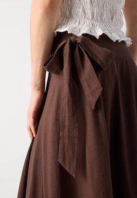 Gonna di lino marrone con un design fluido e un fiocco annodato in vita. Il tessuto ha una consistenza morbida e una leggera lucentezza.