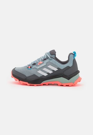 Light blue and dark gray Adidas Terrex trail running shoe with white stripes and coral pink rugged sole, shown from the side.