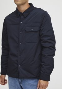 Navy blue jacket in lightweight material, featuring a button-up front, spread collar, and one chest pocket with a flap.