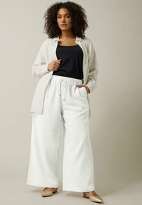 Witte wijde broek met een elastische tailleband, gecombineerd met een zwarte tanktop en een lichte, opengeknopte shirt. Glad stoffen textuur.