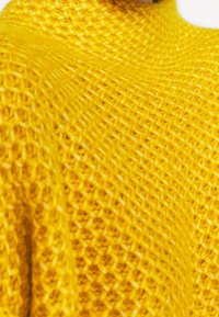 Pull en tricot jaune avec une surface texturée, présentant un encolure large et décontractée et un motif à maille ouverte. Tissu doux.