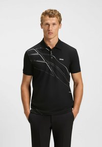 Zwarte poloshirt van gladde stof, met een witte abstracte lijnontwerp aan de linkerkant en een merklogo op de borst.
