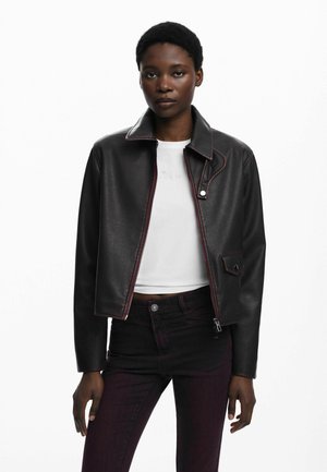 Zwarte nep leren cropped jas met rode stiksels, klassieke kraag, ritssluiting en voorzakdetails, gedragen over een witte top.