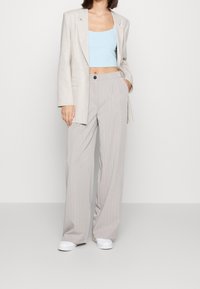 Světlé šedé proužkované kalhoty, volnější střih, zkombinované s přiléhavým světle modrým zkráceným topem a odpovídajícím oversized šedým blejzrem. Bílé tenisky.