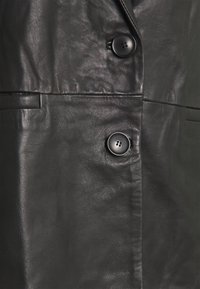 Musta nahkavaate, jossa sileä pinta, kaksi nappia ja räätälöity muotoilu näkyvine taskudetaljeineen.