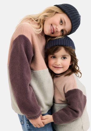 Zwei Kinder tragen farblich abgestimmte Fleece-Pullover in gedämpften Tönen von Rosa, Grau und Lila, kombiniert mit gerippten marineblauen Mützen.