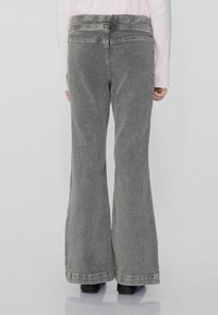 Szare dżinsy w fasonie dzwonów z wysokim stanem, wykonane z denimu. Charakteryzują się czystym wykończeniem, jednolitym kolorem i odsłoniętymi szwami wzdłuż szwów.