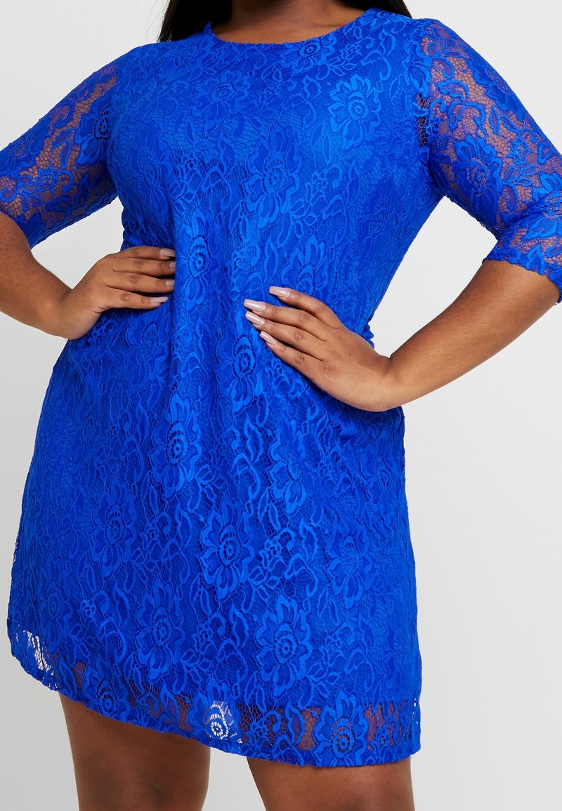 Niebieska koronkowa sukienka z rękawami długości trzy czwarte, w kwiatowe wzory, o luźnym kroju, z okrągłym dekoltem i lekko asymetrycznym dołem.