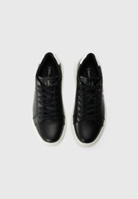 Sneaker in pelle nera con una texture liscia, accenti bianchi sul tallone e cuciture ton sur ton. Presentano lacci neri e un logo sulla linguetta.
