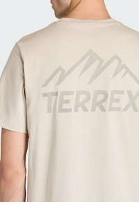 Beżowy bawełniany t-shirt z szarą grafiką gór i napisem "TERREX" na plecach. Klasyczny okrągły dekolt i krótkie rękawy.