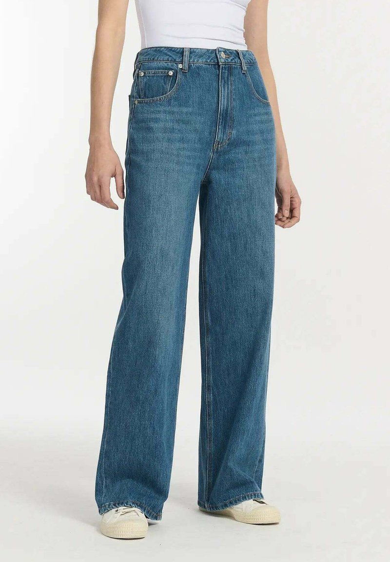 Hogwaist, wijde blauwe spijkerbroek van denim, met een klassieke vijf-pocketontwerp en subtiele vervaging, gedragen met witte sneakers.