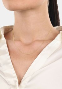 Gul kedja vilar på en bar nacke, kompletterad av en ljusbeige satinbutton-up skjorta med V-ringning.