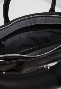 Borsa nera in pelle con compartimento principale parzialmente aperto con cerniera e una tasca interna con cerniera visibile all'interno.