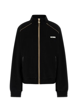 Veste noire zippée avec fermeture éclair dorée, poignets et ourlet élastiques, et logo blanc « GUESS » sur la poitrine gauche.