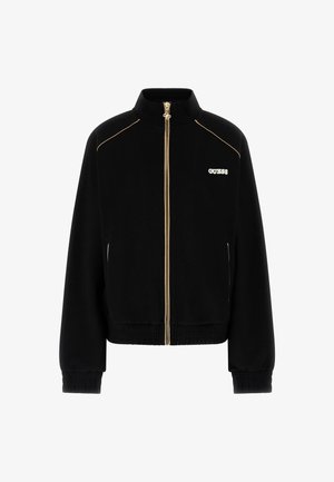 Zwarte jas met ritssluiting, gouden ritssluitingrand, elastische manchetten en zoom, en een witte "GUESS"-logo op de linkerborst.