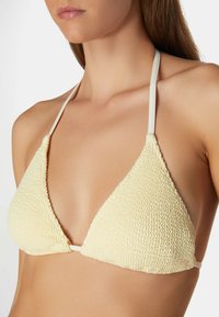 Geel, getextureerd triangeltopje met dunne witte bandjes. Opvallend door de textuur van de stof en het minimalistische ontwerp.