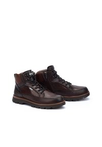 Leather hiking boots in dark brown with a lace-up front and side zipper. Features a textured toe cap and a rugged rubber sole for traction.