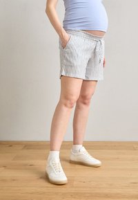 Shorts rayés en coton bleu clair et blanc avec une taille à cordon et des poches latérales, associés à des baskets blanches et des chaussettes.