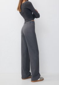 Wide-leg gray trousers with a textured finish, high waist, and front pleats, paired with casual footwear. Back view displayed.