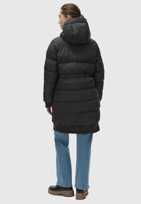 Black puffer coat with a hood, featuring horizontal stitching and a cinched waist. Paired with light blue jeans and black platform shoes.