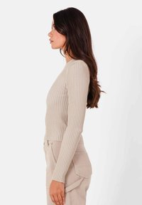 Långärmad, beige ribbad stickad topp med en figurnära passform, rund halsringning och subtil textur, tillsammans med ljusa, högmidjade byxor.